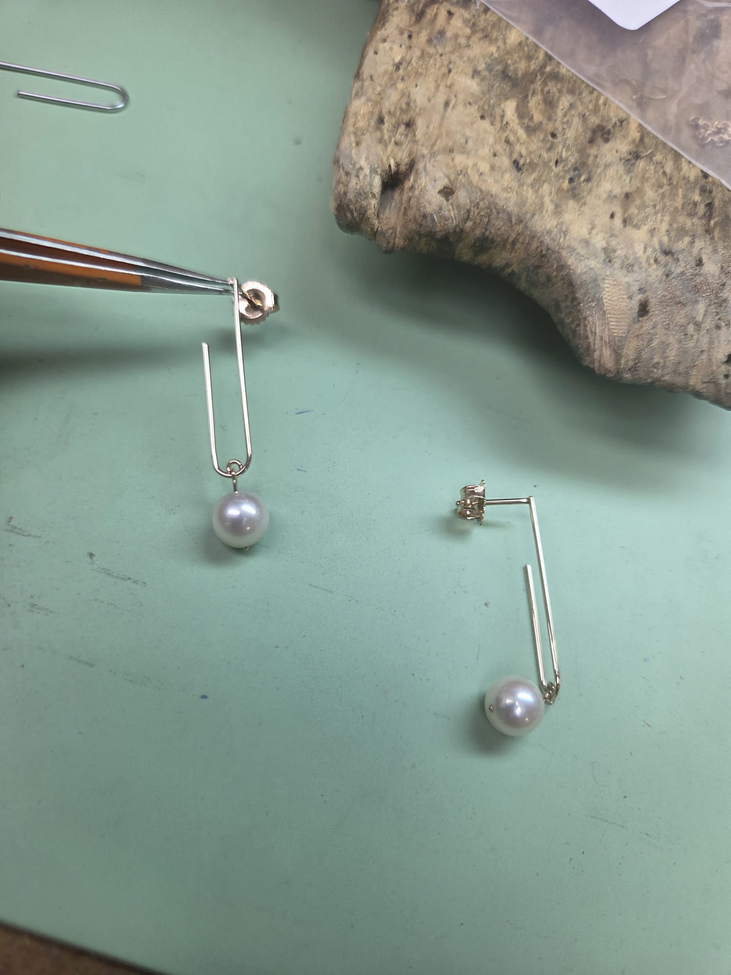 A pair of custom designed pearl earrings hanging on a pair of pliers
