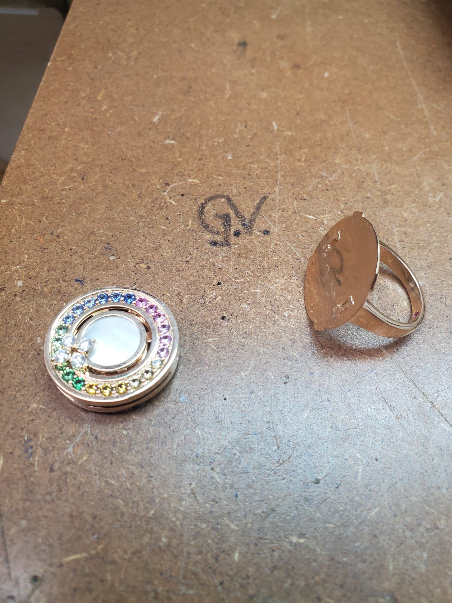 A pendant set with rainbow gemstones laying on a table next to a gold ring body