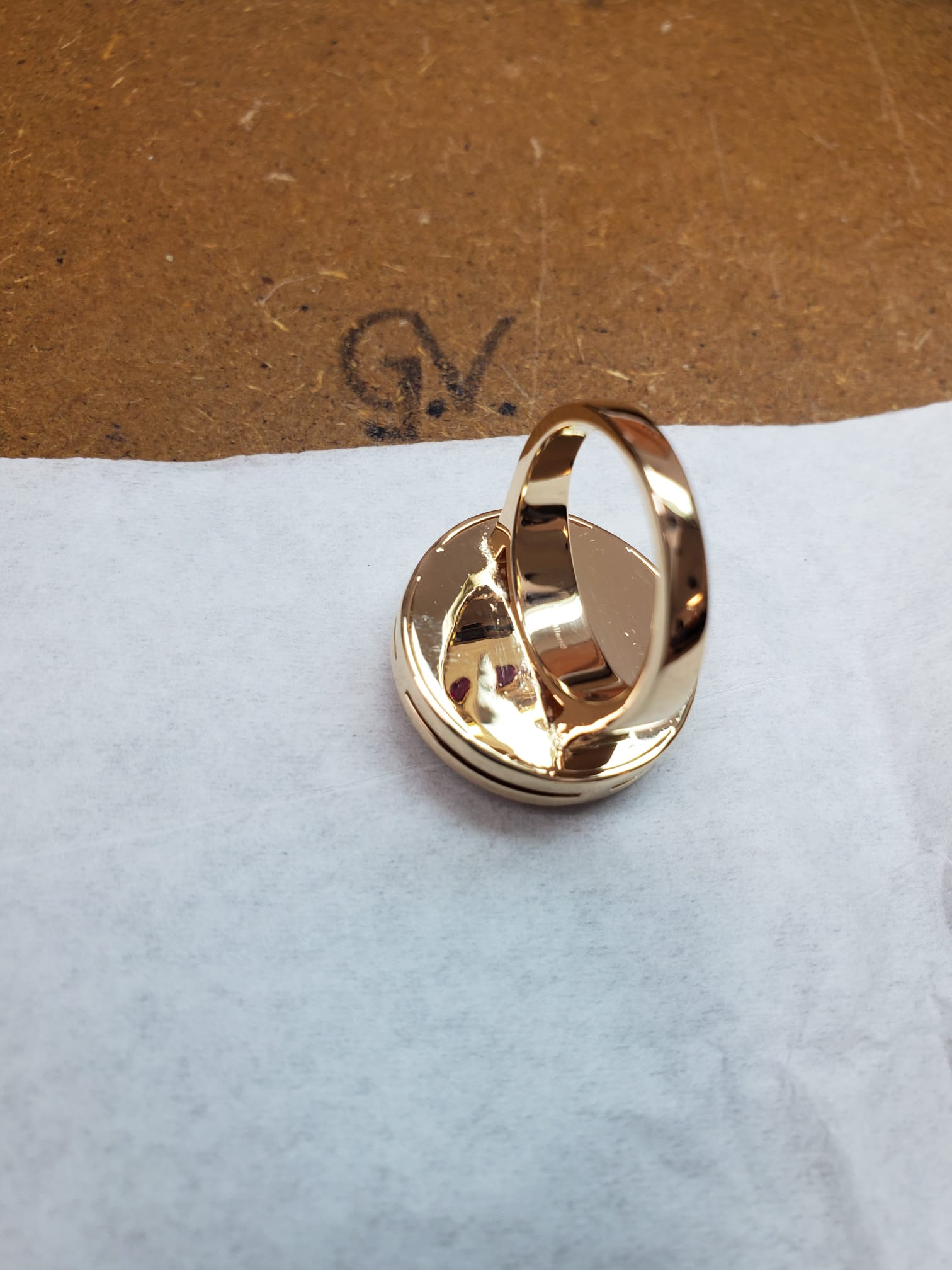 A gold ring shank jutting out from the back of a pendant on a workspace table