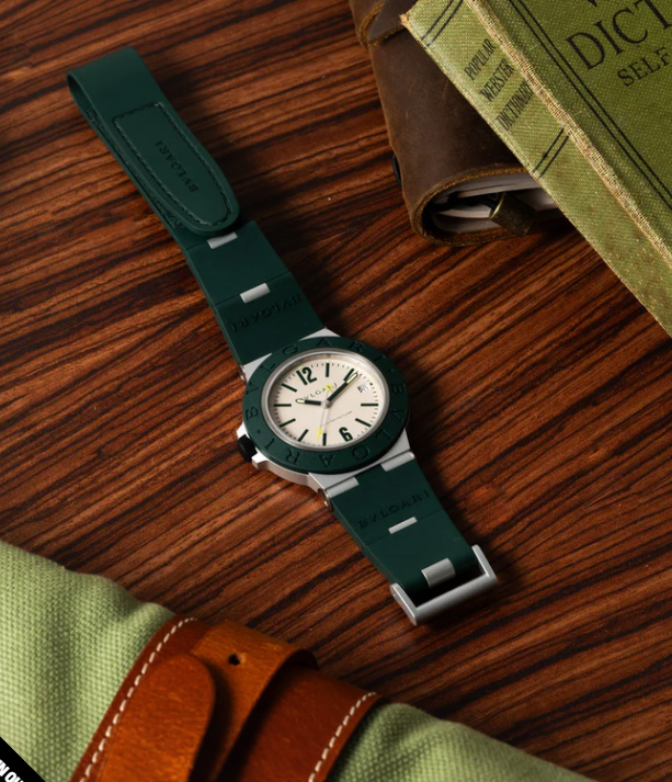 A dark green watch with a white dial laying on a striated wood table
