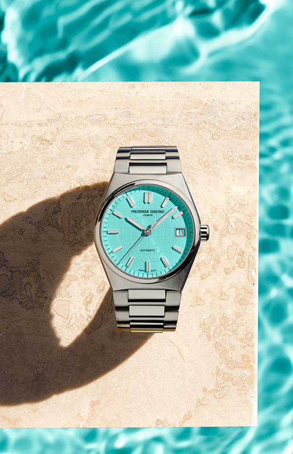 A silver watch with a light teal dial, sitting on a beige marble slab over a pool surface