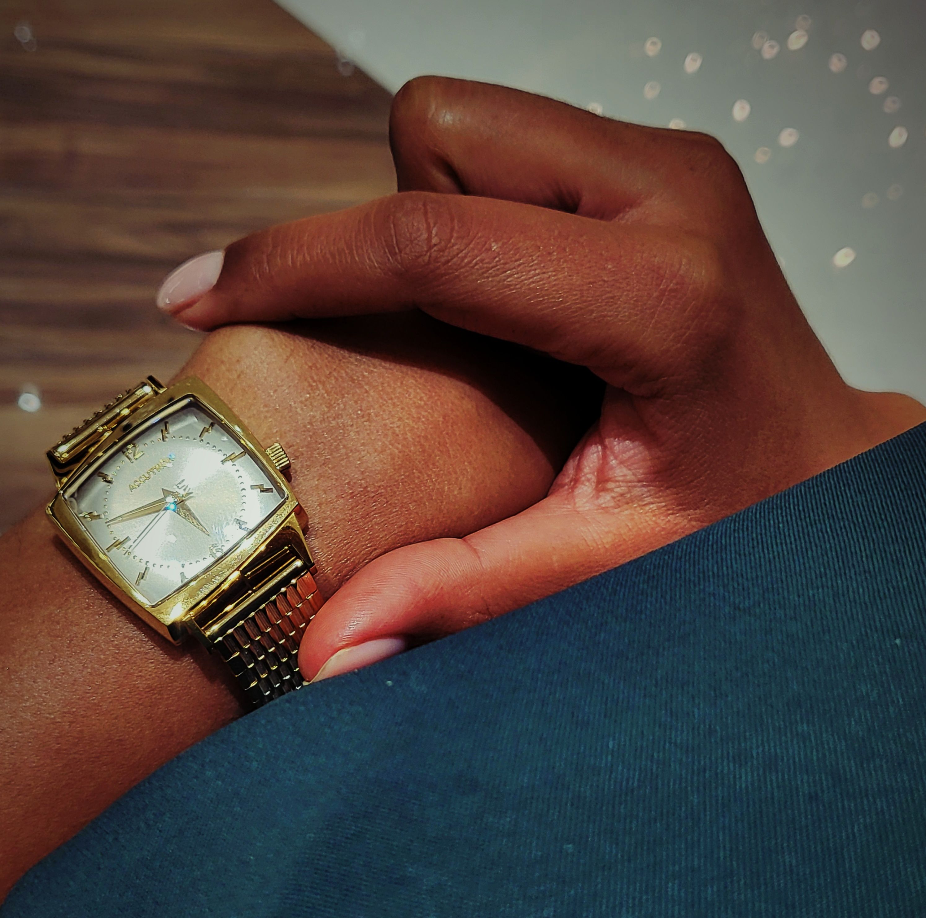 A brown-skinned female hand framing a gold watch with the fingers
