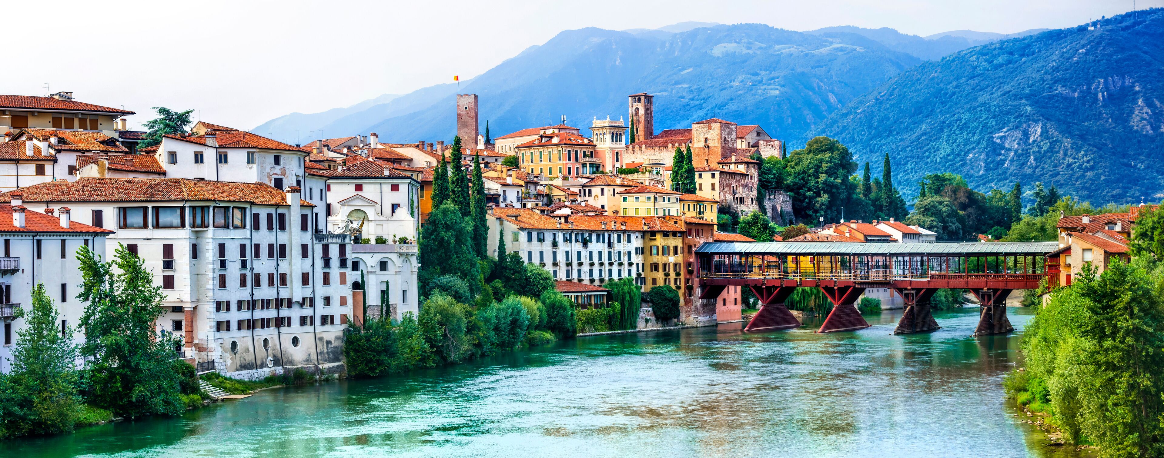 Vicenza, Italy. A white and red cluster of buildings with a covered bridge over water in front of mountains.