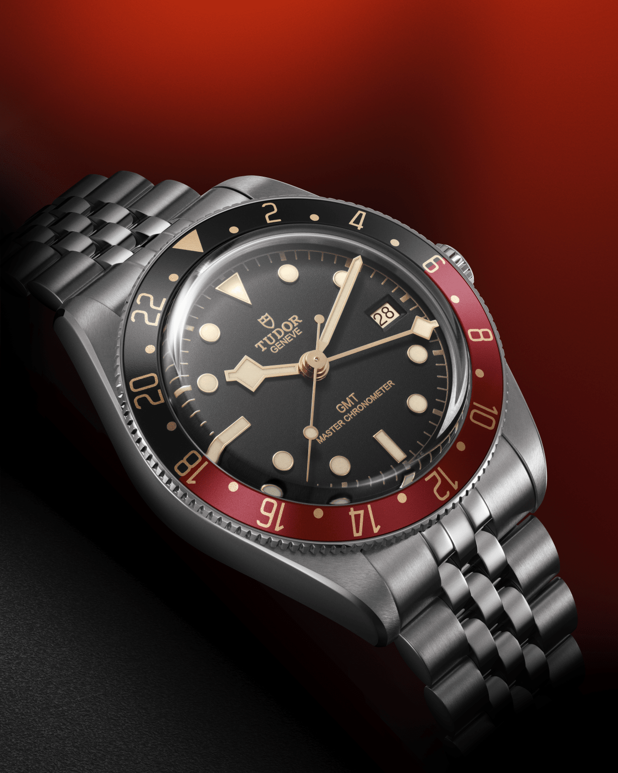 A stainless steel watch on a bracelet with a two-tone black and burgundy bezel with a black dial. Gold details decorate the bezel, dial and hands.