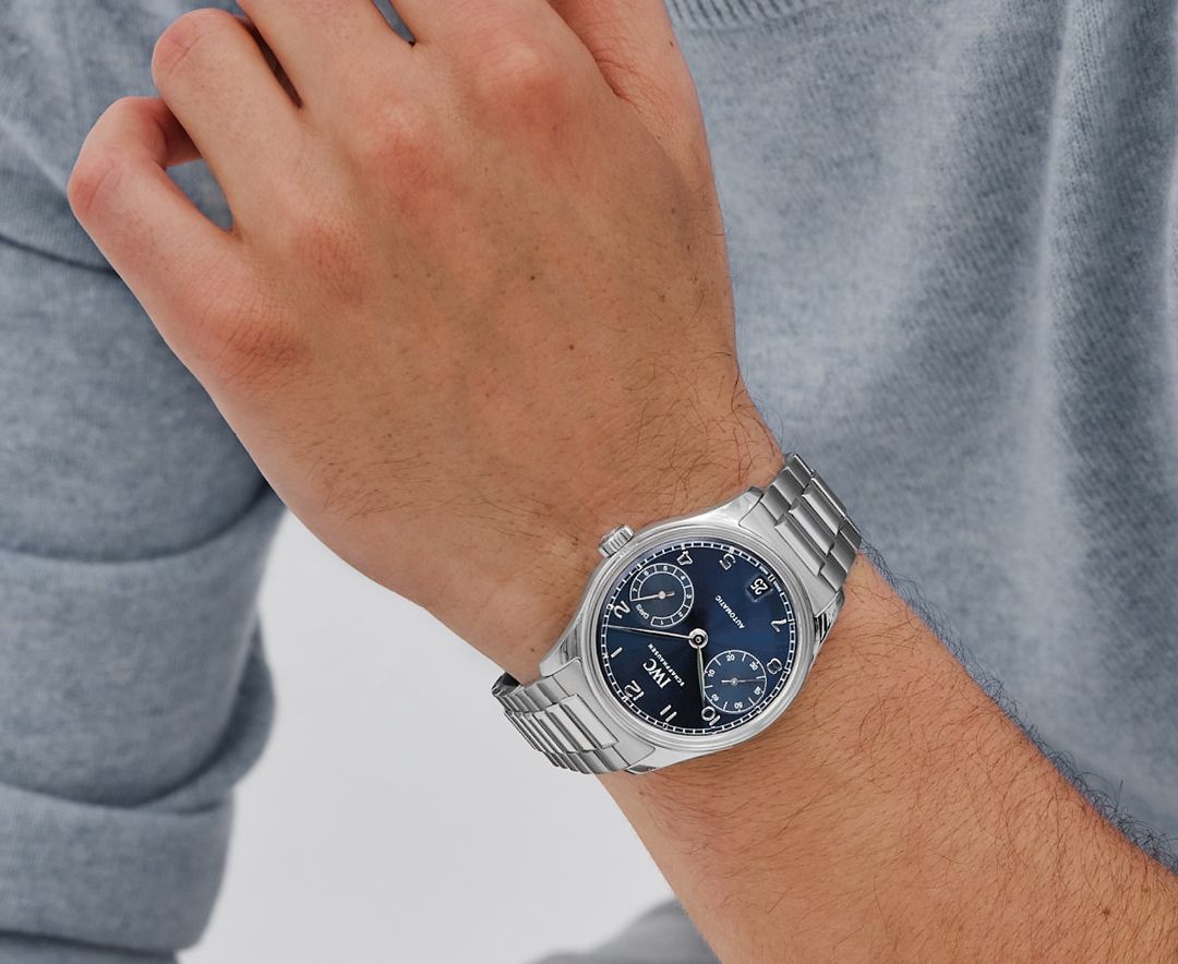 On a white man's wrist, a stainless steel watch with a dark blue dial and 2 sub-dials. Appliques are white, and bezel is smooth.