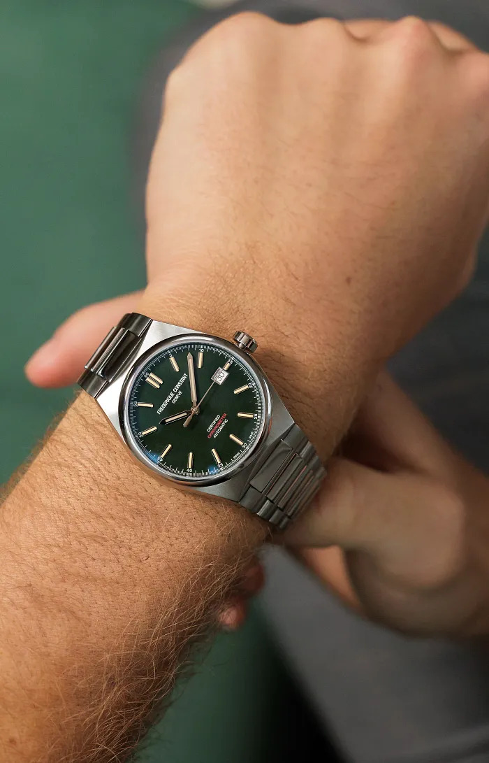 A stainless steel Frederique Constant watch with a dark green dial and stick markers, on a man's wrist