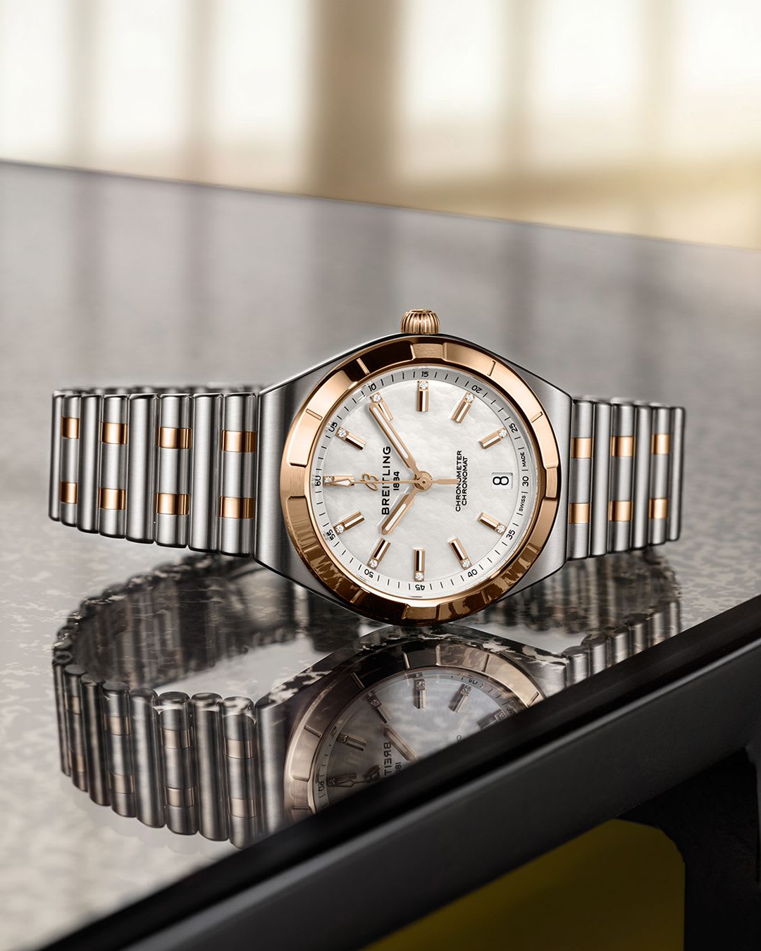 On a dark marble counter, a stainless steel and rose gold watch with mother of pearl dial and gold stick markers